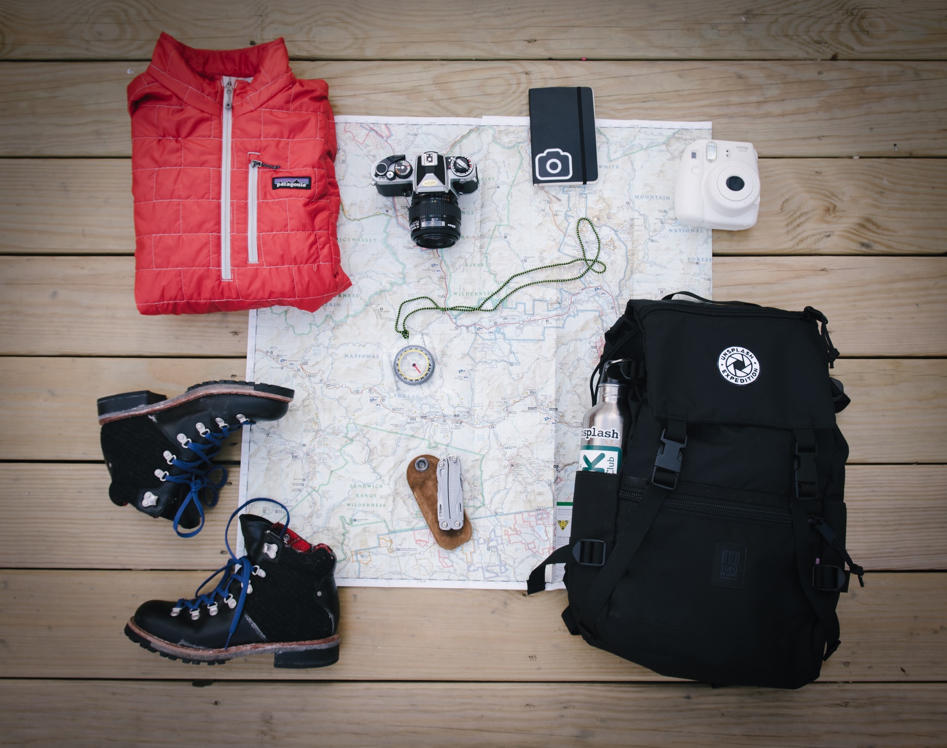 a backpack unpacked to show tools like a map, a compass, a camera, etc